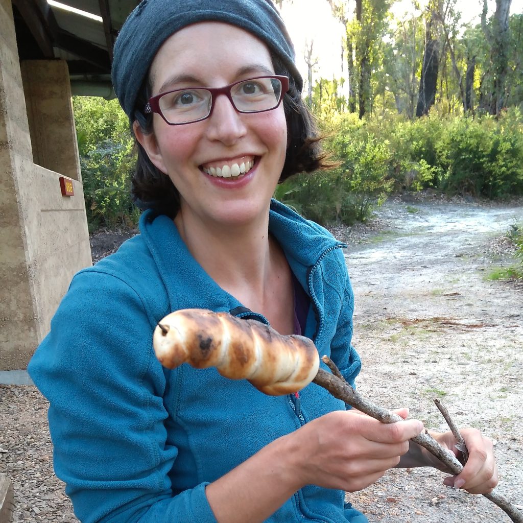Frau mit Stockbrot auf einer Trekkintour